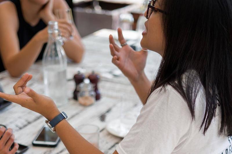 conversation A woman speaks with hand gestures at a table.