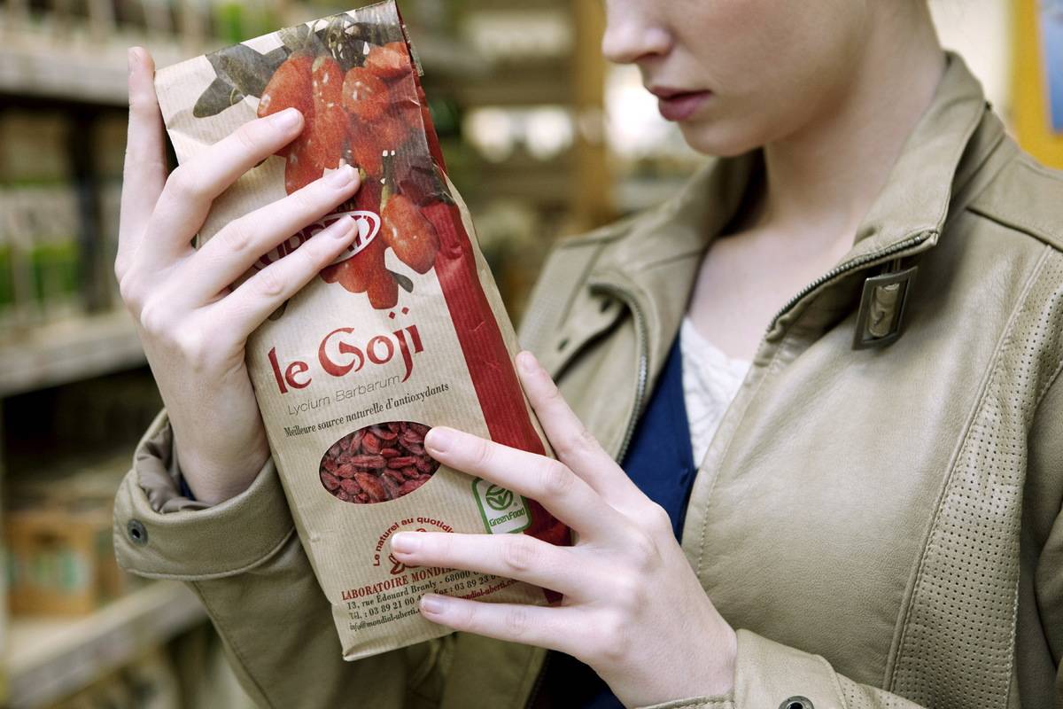 A woman holds up a bag of goji berries in an organic supermarket.