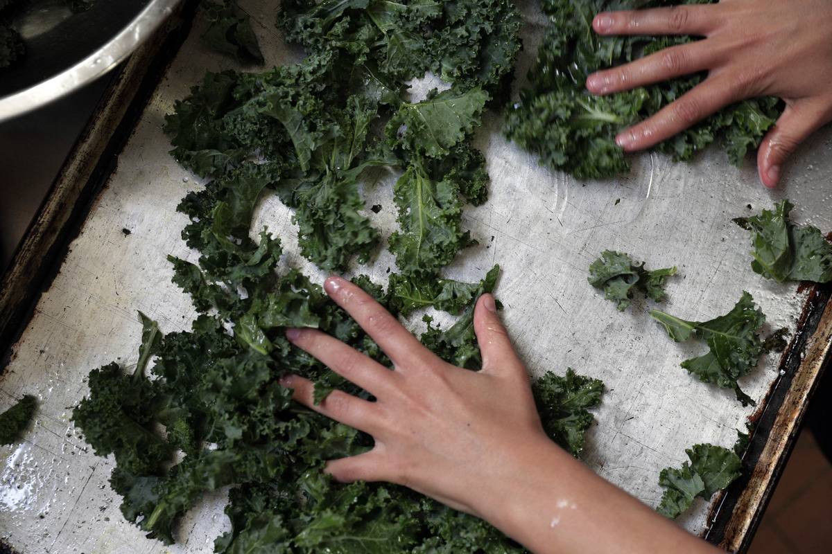 A woman rubs kale with olive oil before putting it on a baking pan.