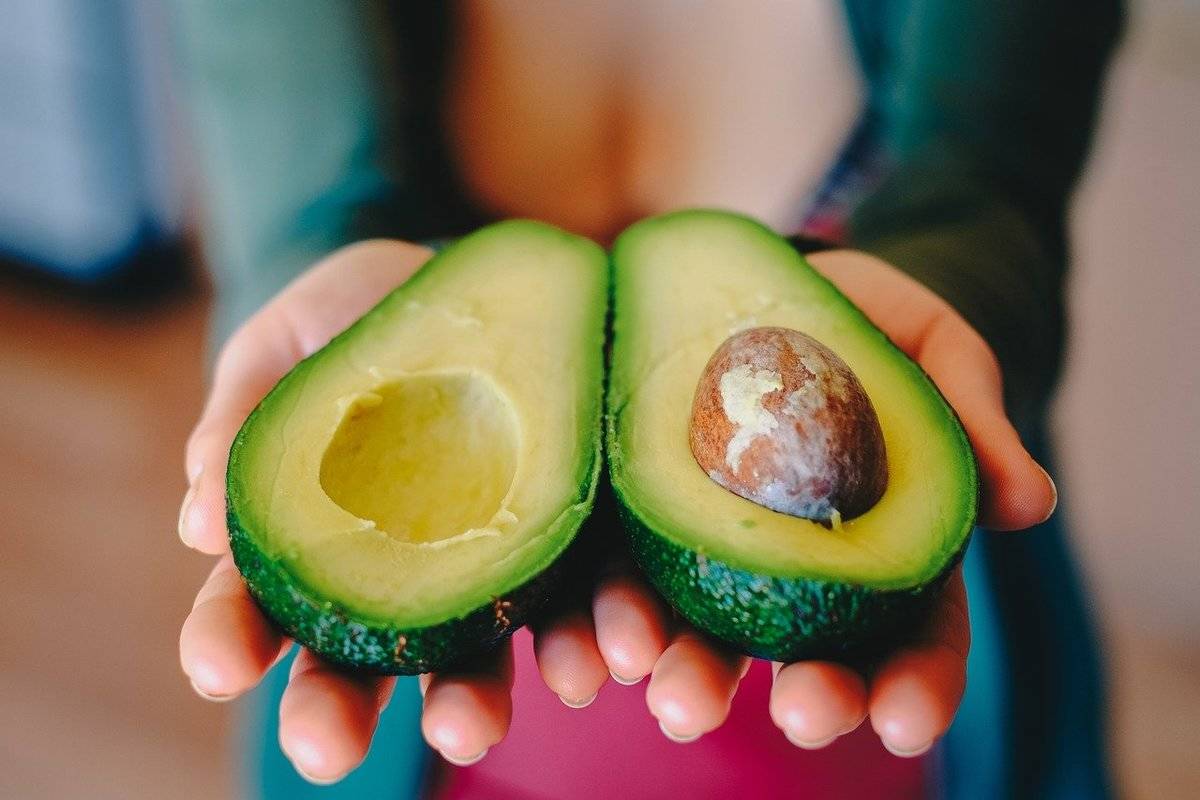 A woman holds two halves of an avocado.