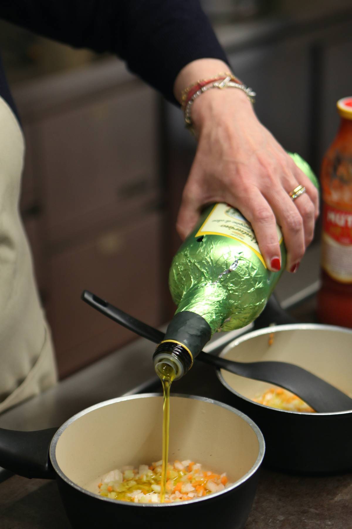 A chef pours olive oil into a pot full of vegetables.