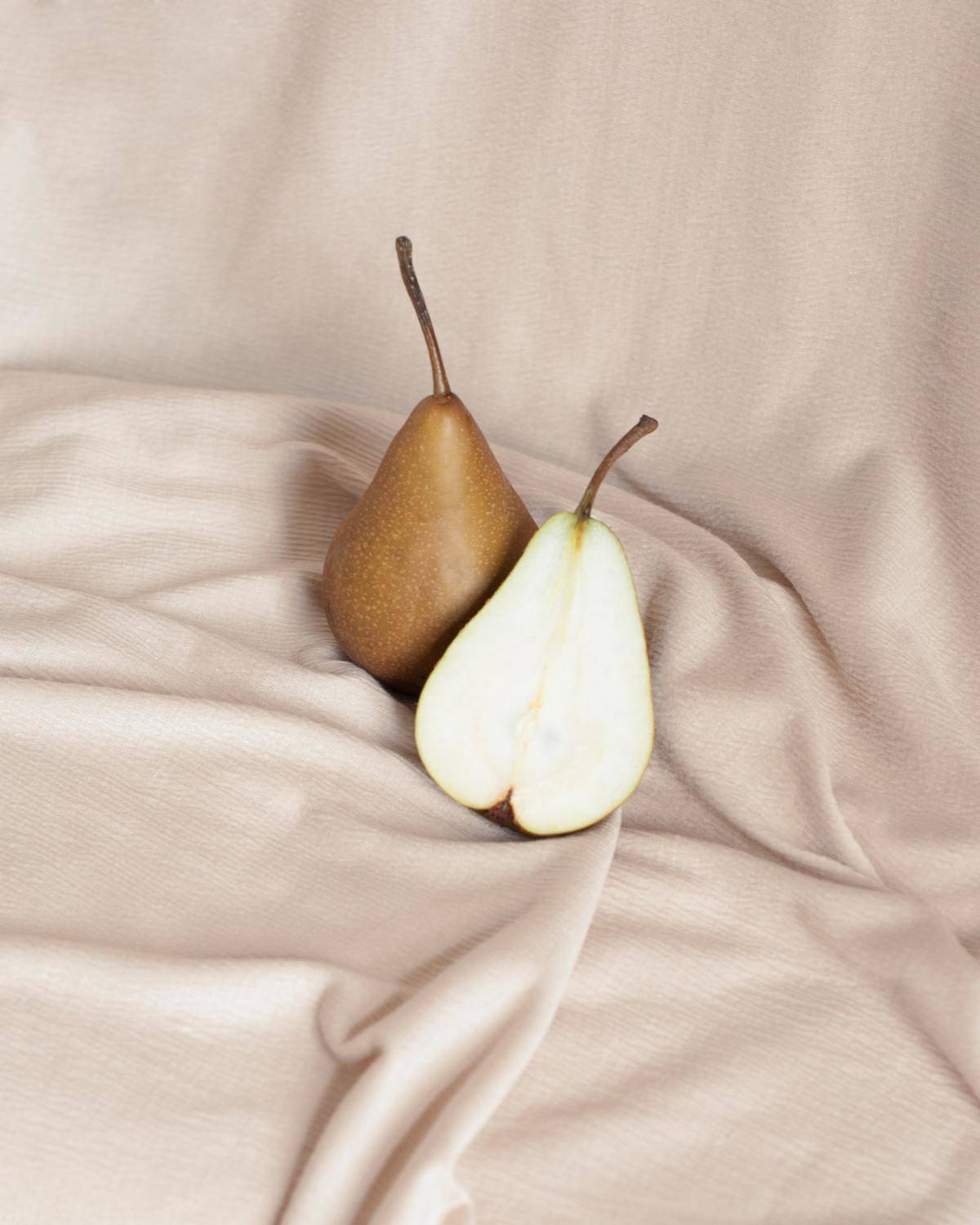 A whole and half pear sit on a brown cloth.