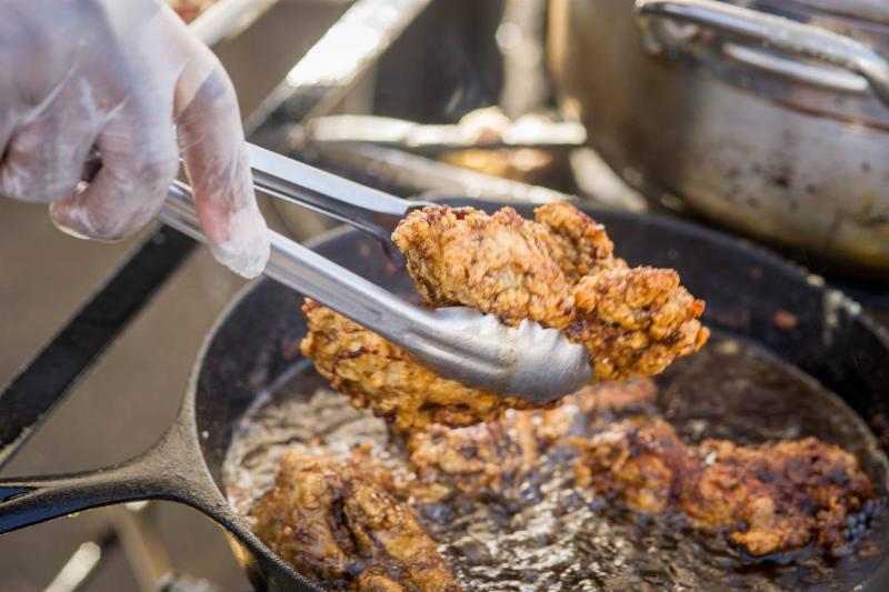 Close-up of tongs pulling out fried chicken from a cast iron pan Close-up of tongs pulling out fried chicken from a cast iron pan