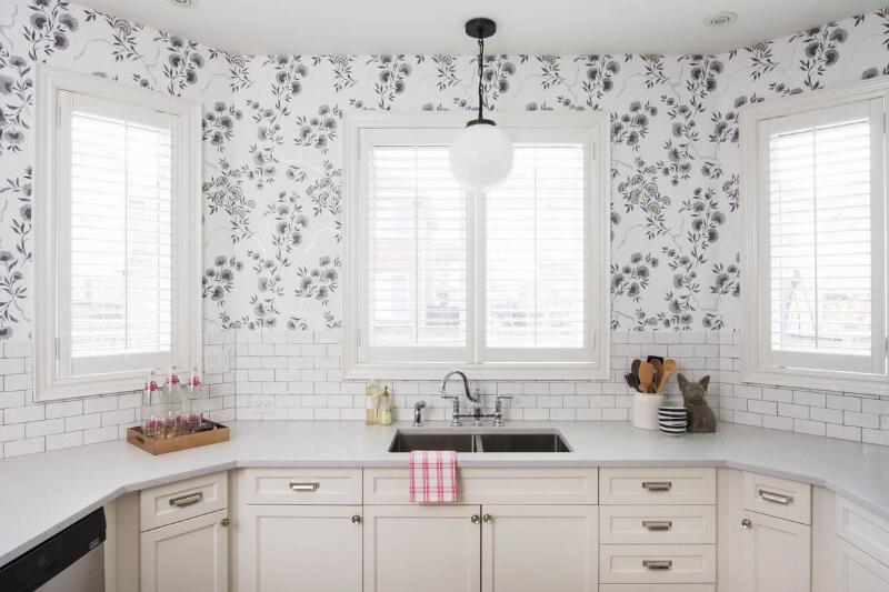 A modern kitchen has an accent wall with floral wallpaper.