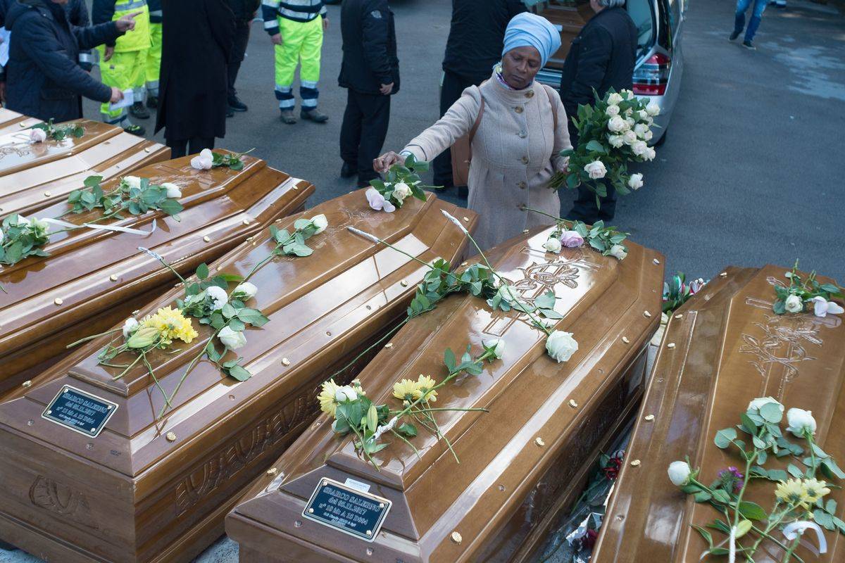 coffin flowres A woman lays flowers on coffins placed next to each other.