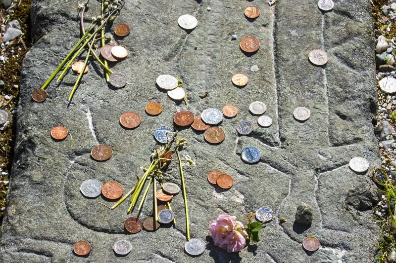 A variety of coins sit on a tombstone.