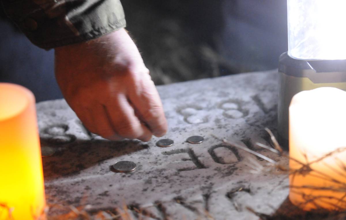 placing coins on grave A visitor places coins on a grave marker.