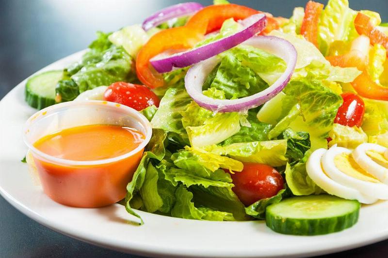 dressing 491623328 Salad with a side of devilled eggs. Slices of white and yellow deviled eggs sit on a plate with a small cup of dressing