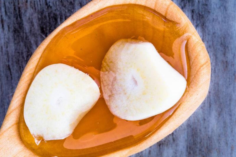 garlic 904782894 honey with garlic served on a rustic wooden spoon and over a marble cutting board