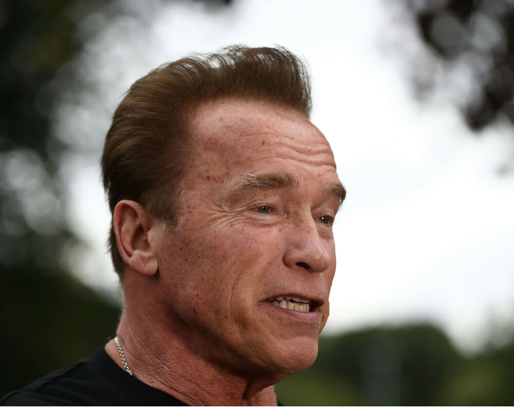 Arnold Schwarzenegger wearing black t-shirt, speaking outside