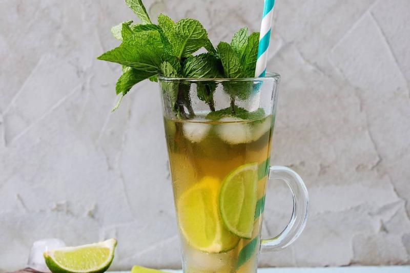 Glass of Iced green tea with lime, lemon, mint and ice cubes on wooden chopping board over light blue textured background with green textile napkin. Glass of Iced green tea with lime, lemon, mint and ice cubes on wooden chopping board over light blue textured background with green textile
napkin.