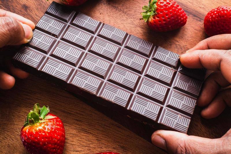 hand gripping dark chocolate bar next to strawberries