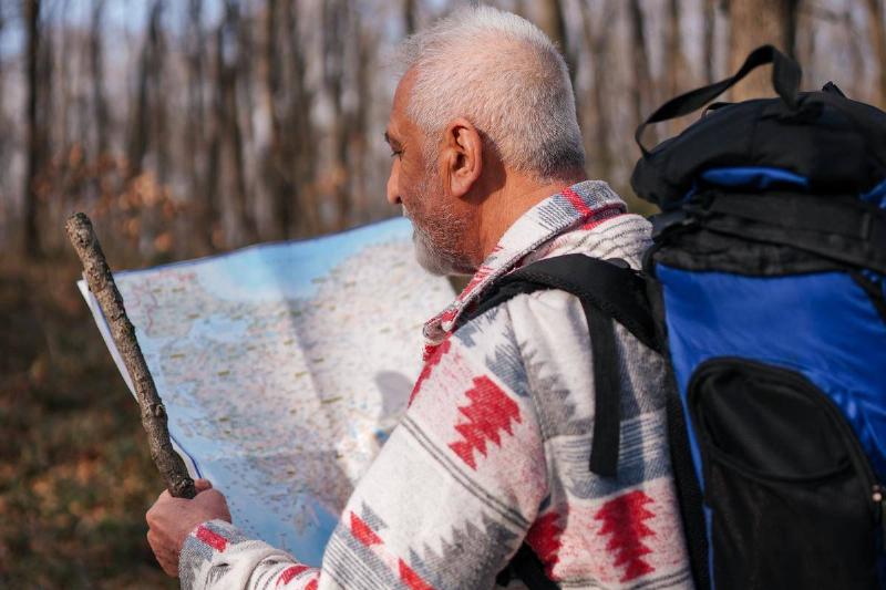 Man with walking stock holding peper map in woods Man with walking stock holding peper map in woods