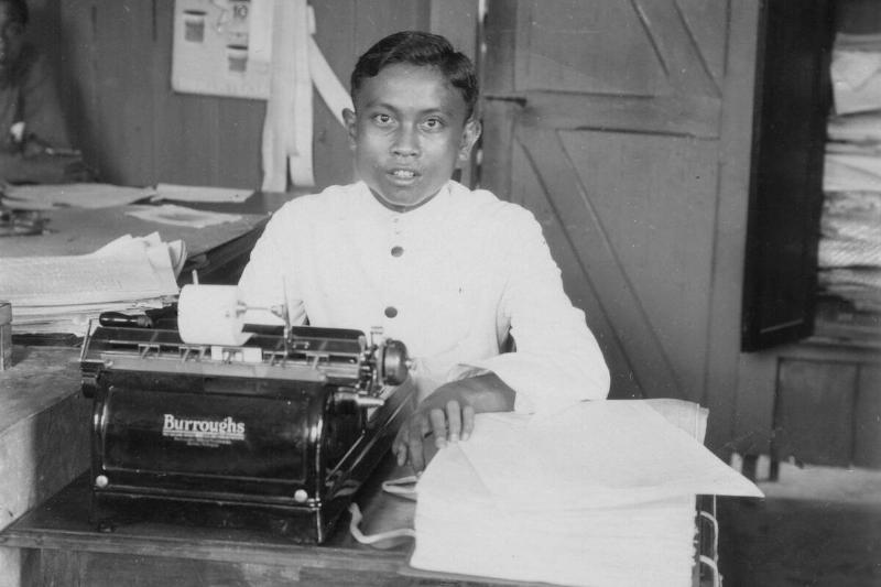 A young man sitting at a typewriter, Indonesia, 20th century. A young man sitting at a typewriter, Indonesia, 20th century.