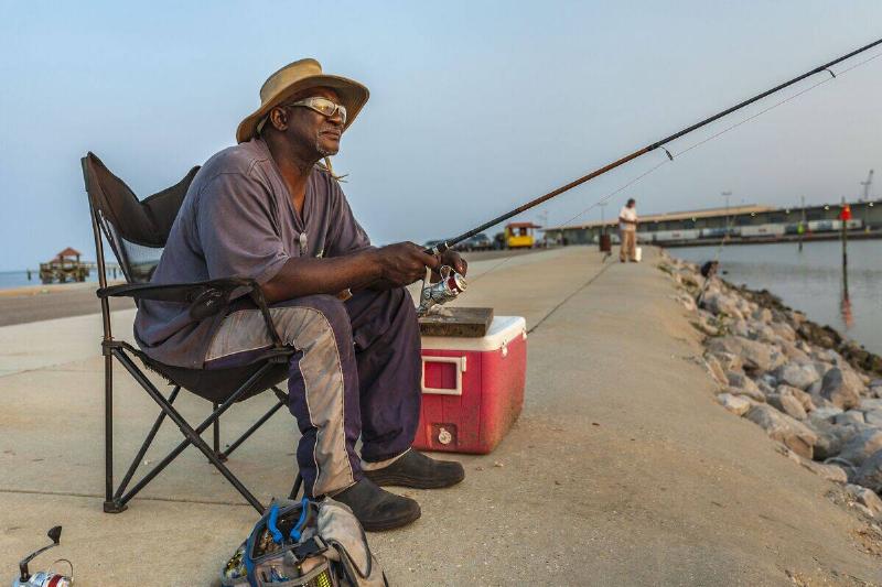 Black man with sunglasses fishing on the jetty at the Gulfport Municipal Marina in Gulfport, Mississippi Black man with sunglasses fishing on the jetty at the Gulfport Municipal Marina in Gulfport, Mississippi