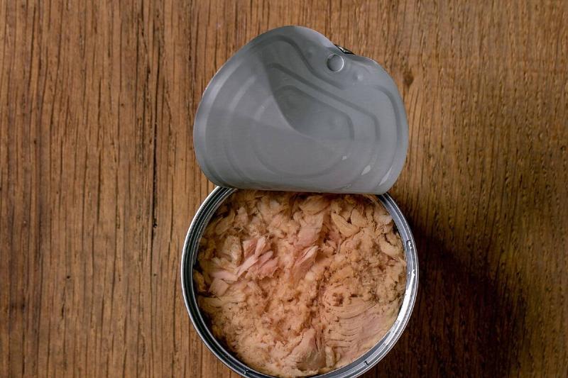 Canned tuna fish in oil in opened can over wooden background, Top view, copy space