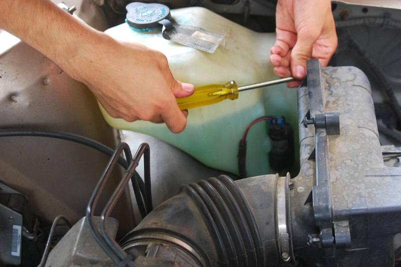 A mechanic working on a Buick automobile, using a screwdriver. A mechanic working on a Buick automobile, using a screwdriver.