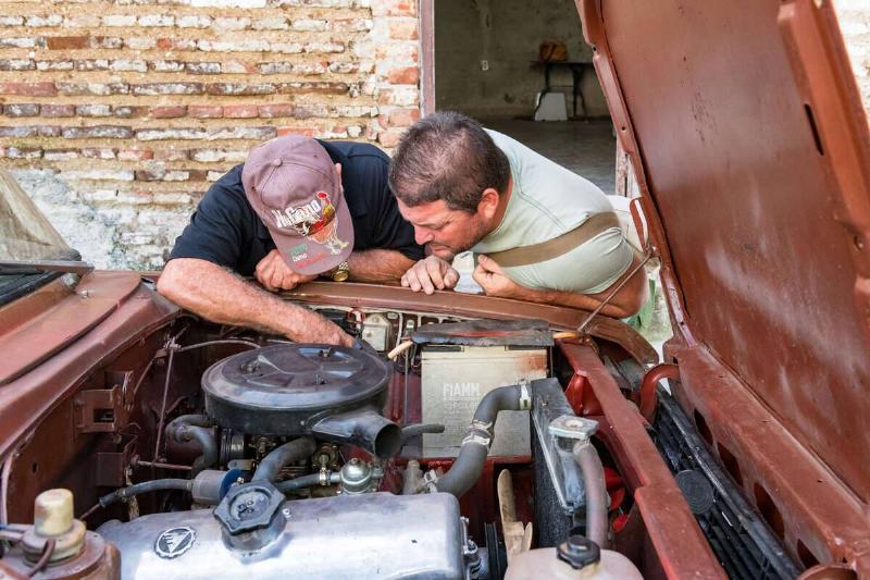 Two Cuban men repairing a car in the city street. It is a... Two Cuban men repairing a car in the city street. It is a...