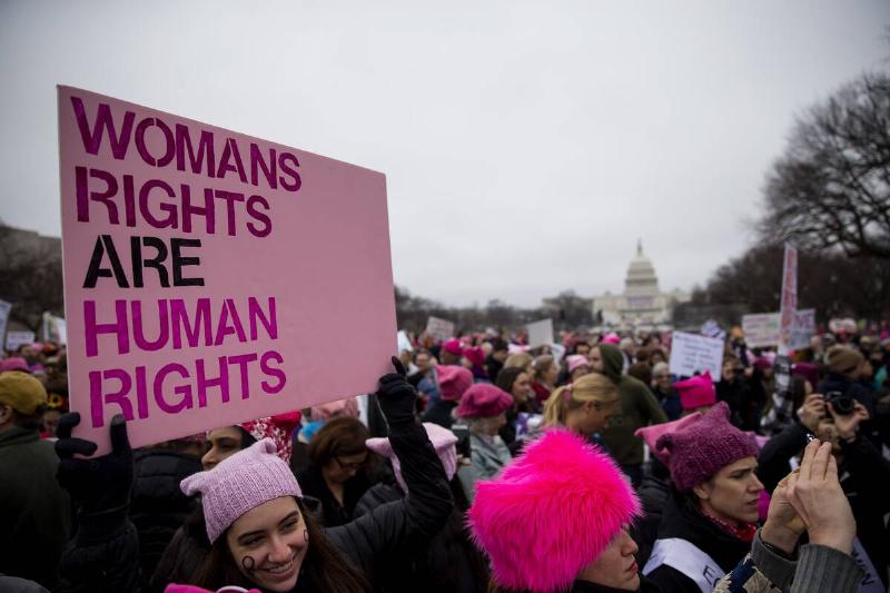 Large crowd standing near the White House, with a woman holding a sign reading, 
