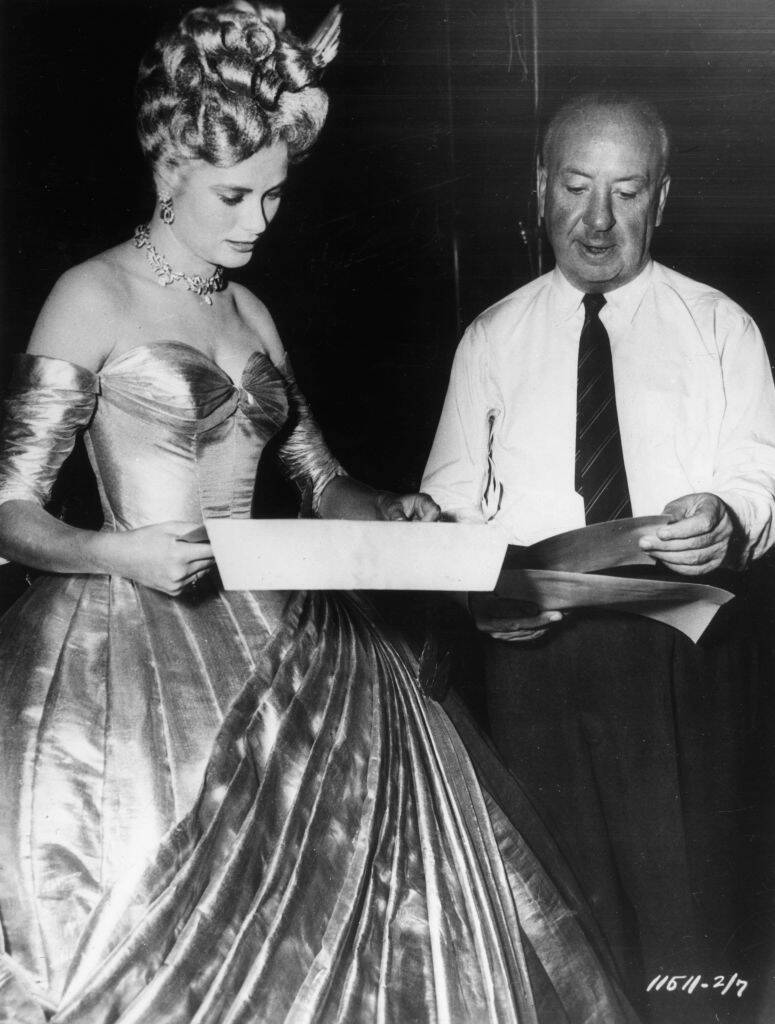 Grace Kelly and Alfred Hitchcock standing together, looking at items in their hands