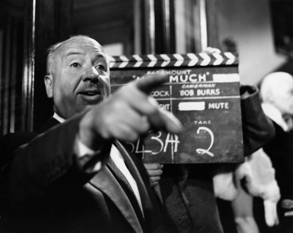 Alfred Hitchcock standing on a film set, pointing to something off-camera