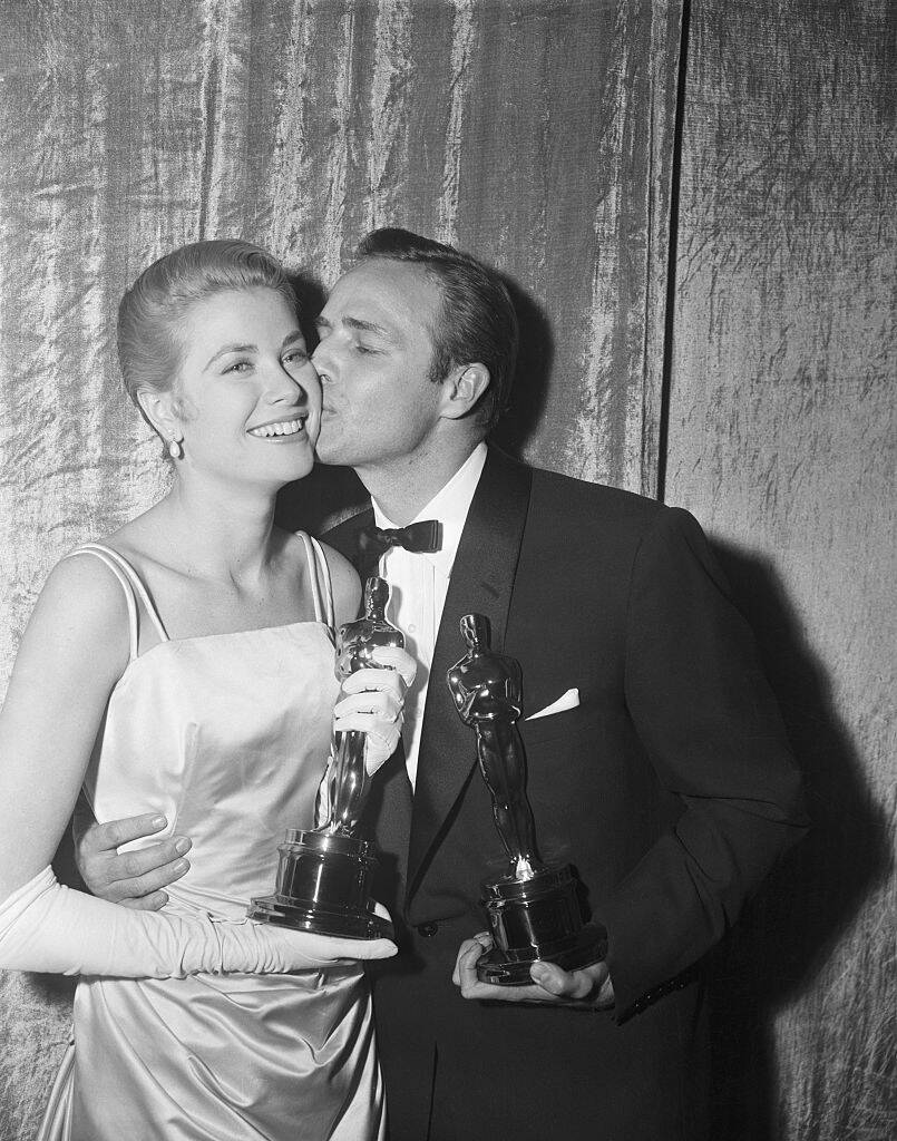 Marlon Brando kissing Grace Kelly's cheek. They're both holding Academy Awards