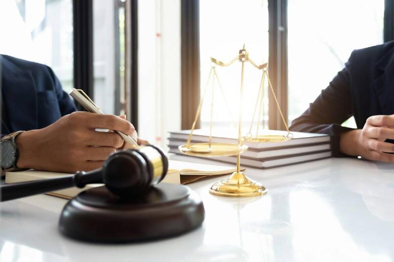 Two individuals sitting at a table that has atop it a gavel, books and the symbol for the weight of justice