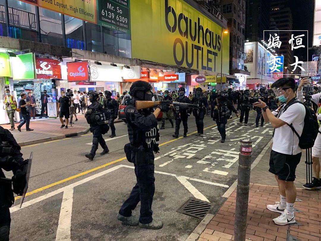 Chinese police and Hong Kong journalists flex their weapons at each other.